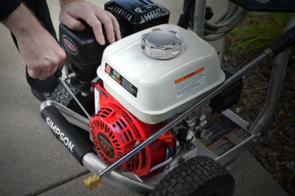 Man pulling the starter cord on a SIMSON® premium pressure washer with his other hand on top of the machine