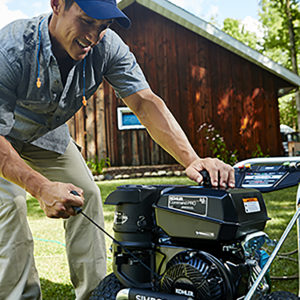 Man starting a KOHLER engine SIMPSON pressure washer in front of a cabin
